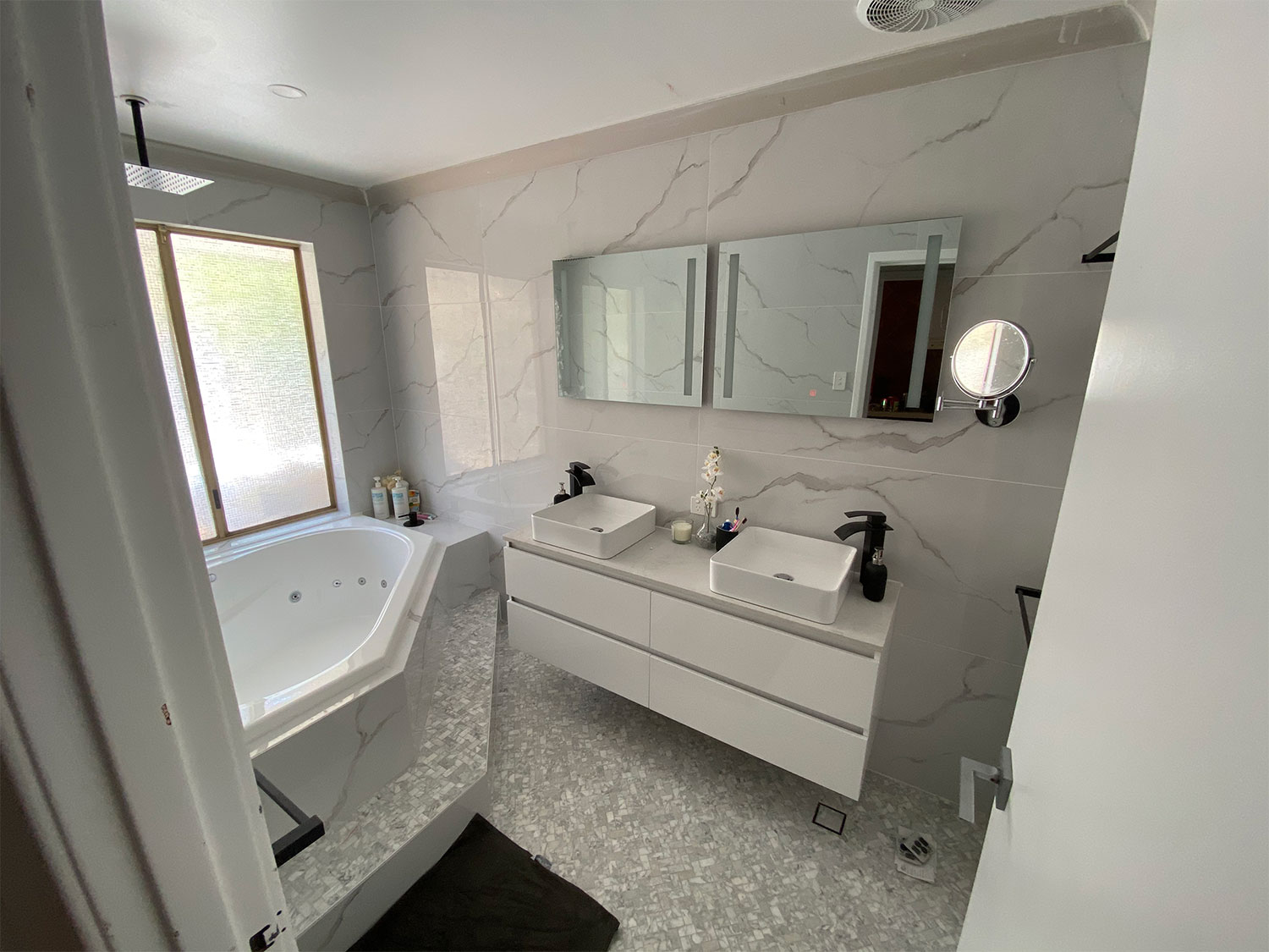 Bathroom with corner bathtub, large mirrors, and natural lighting.